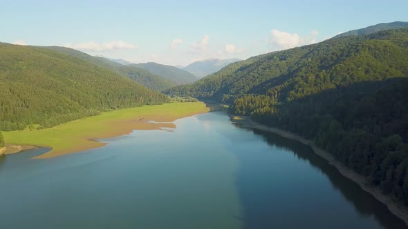 Aerial view of big lake with clear blue water between high mountain hills covered with dense