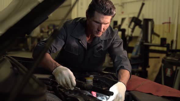 Auto mechanic man standing at the opened hood and lighting with lamp while working