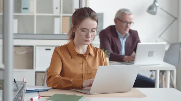 Young Caucasian Woman Working on Laptop in Office and Smiling Anxiously