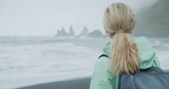 Rear Close Up of Woman on a Black Sand Beach Enjoying View to Reynisfjara Sea Stack Cliff Formations
