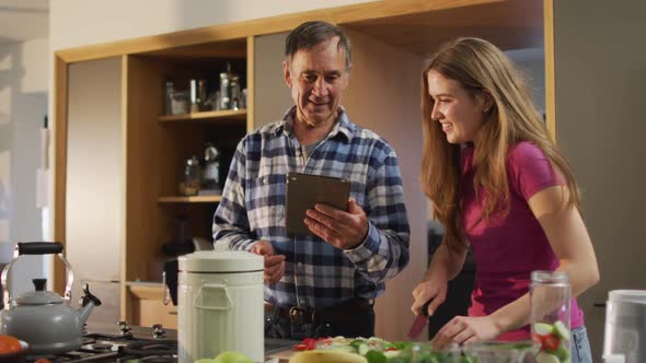 Smiling caucasian senior father with teenage daughter preparing food and using tablet in kitchen