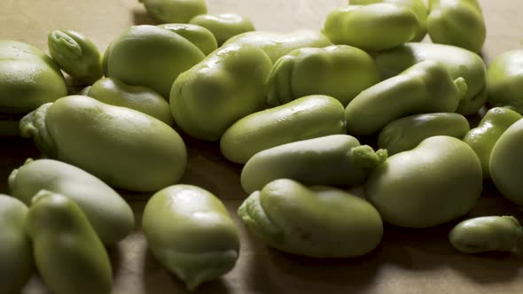 Wide, slider shot from left to right of a bunch of green, sweating fava beans on a wood cutting boar