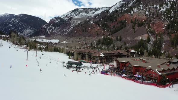 Skiing resort building complex with cable lift and happy people ski, aerial drone view during snowfa