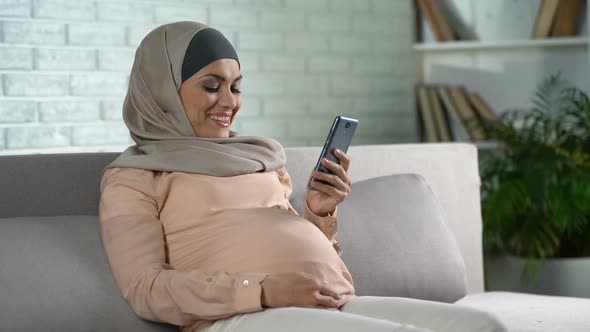 Muslim Pregnant Female Watching Video on Smartphone Home, Expecting Childbirth