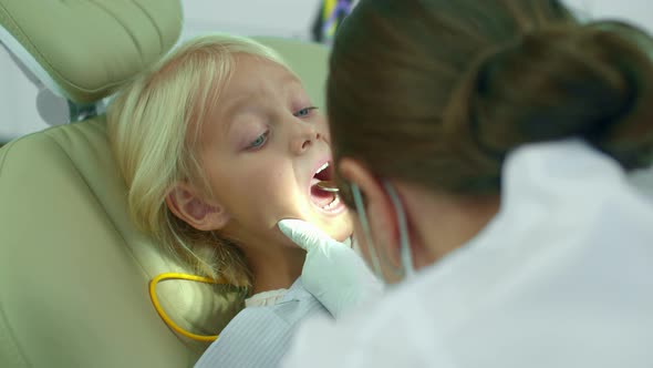 Dentist in Put a Light on Girls Mouth and Looks at Her Teeth.