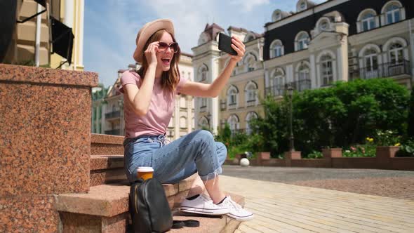 Beautiful Young Woman Tourist with Takeout Coffee Sitting on Stairs Using Smartphone