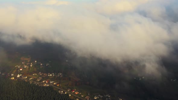 View from above of vibrant landscape of foggy clouds covering mountain hills and village