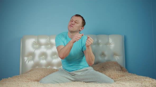 Man Having Fun While Sitting on the Bed Raised His Hands and Dancing Sitting in Front of Camera