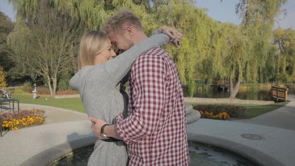 Medium shot of a happy attractive couple talking and hugging in front of a park fountain in Autumn