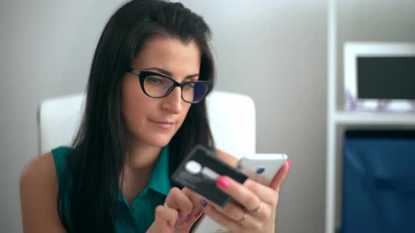 Woman Entering Data Using Smartphone While Holding a Credit Card in the Other Hand