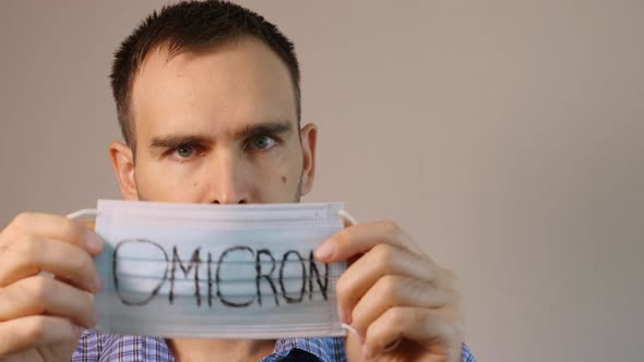 A European man in a blue plaid shirt puts on a medical mask with Omicron written on his face
