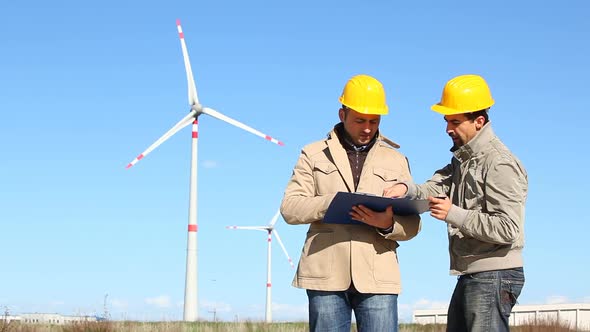 Two Engineers at Work with Wind Turbine on Background