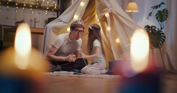 Father and Daughter Wearing Crowns Playing in Toy Wigwam at Home