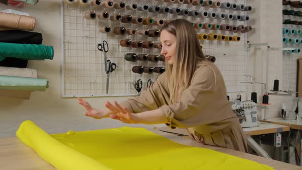 Close up of female designer unwinding a big yellow roll of fabric tissue on table at design studio