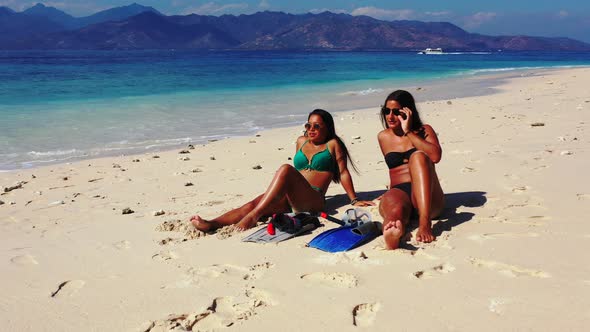 Young smiling ladies relaxing having fun on the beach on paradise white sand and blue 4K background