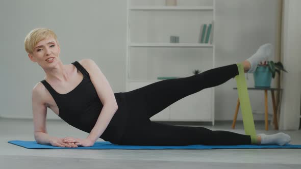 Middleaged Caucasian Woman Online Trainer Wears Black Tracksuit Lies on Mat Floor at Home Doing