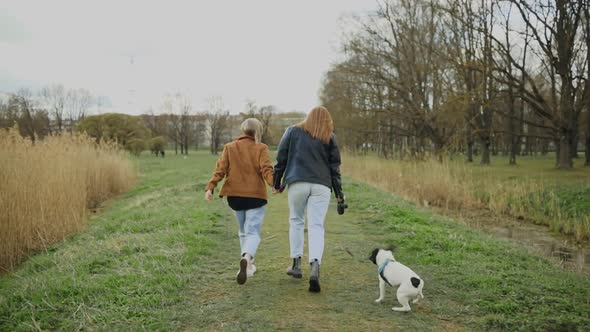 Female LGBT Couple Running Away and Playing with French Bulldog in Park