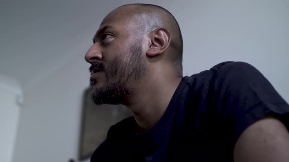 Bald UK Asian Male Watching TV Off Screen Expressively With Eyes. Low Angle, Locked Off