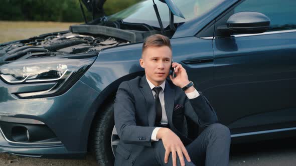 Upset Businessman Use Phone Sitting on Road Near the Broken Car