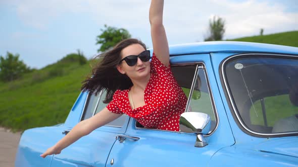 Young Girl in Sunglasses Leaning Out of Vintage Car Window and Enjoying Trip