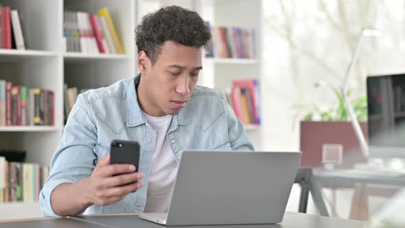 Young African American Man Working on Smartphone and Laptop 