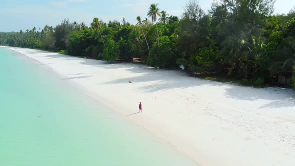 Aerial Slow motion: woman walking on white sand beach turquoise water tropical coastline