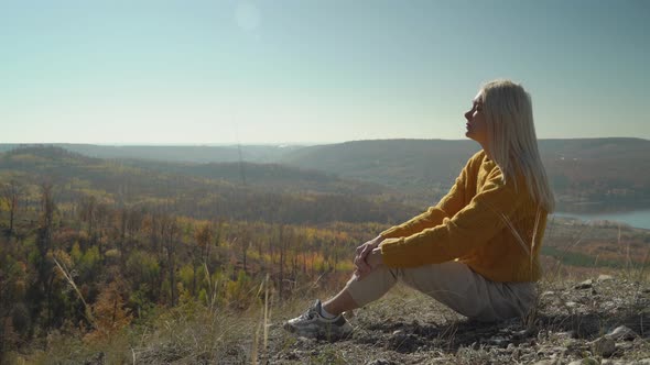 Young woman sits on stones and enjoys the autumn warmth in the mountains