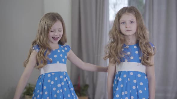 Two Identical Twin Sisters with Different Temperament Types Posing at Home. Cheerful Girl Jumping Up