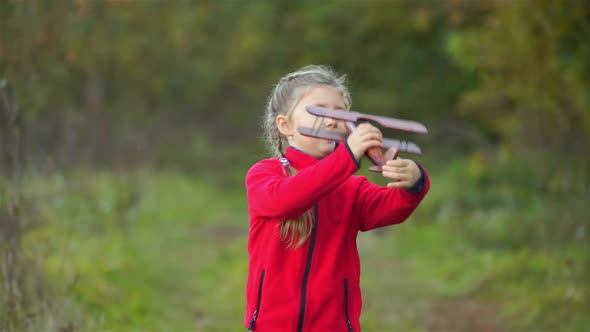 A little girl  in the background of nature playing a wooden toy plane.