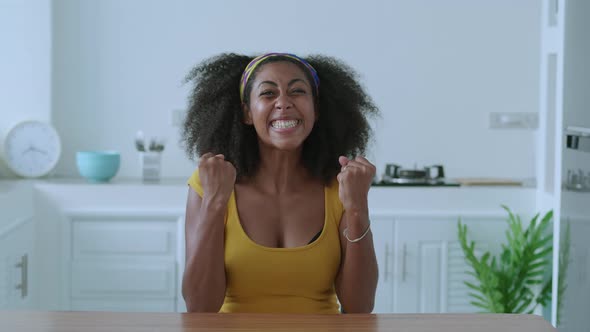 Focus on Facial Expression of a Happy African Woman Looking at Camera Sitting at Wooden Table at