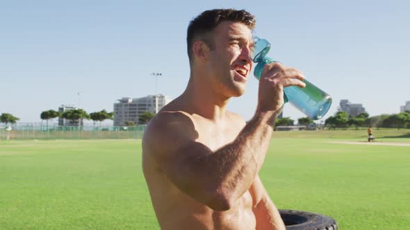 Fit shirtless caucasian man dinking water after exercising outdoors