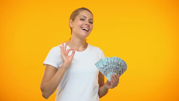 Positive Female Showing Ok Gesture Holding Dollars in Hand, Financial Investment