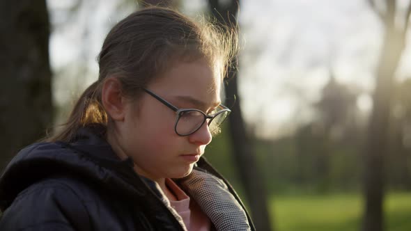 Closeup Pretty Girl Sitting in Sunny Park. Teenager Girl Reading Outdoors