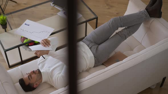 Wide Shot Top View of Concentrated Young Middle Eastern Man Writing Down Ideas in Sketchbook Lying