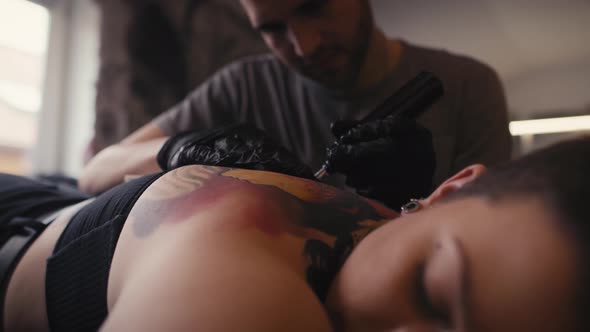 Focus caucasian man tattooing woman at the studio. Shot with RED helium camera in 8K.