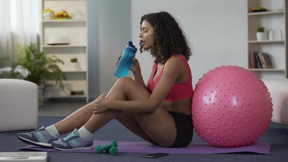 Young Woman in Sportswear Sitting on Floor, Drinking Water from Bottle, Workout