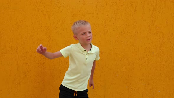 A Little Cheerful Boy Jumps and Has Fun Against the Background of a Yellow Wall