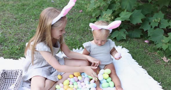 Two Children Wearing Bunny Ears When Pick Up Painted Easter Egg Hunt In Garden or Park