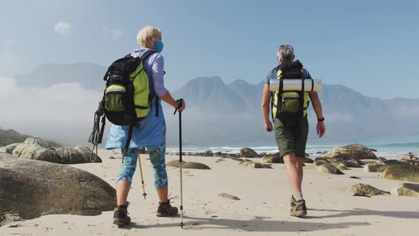 Rear view of senior hiker couple wearing face mask with backpacks and hiking poles