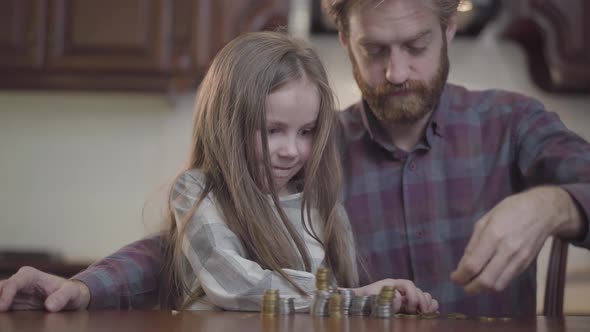 Close-up Portrait of Bearded Man Sitting at the Table in the Kitchen with His Daughter Counting