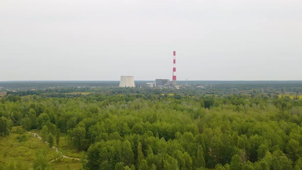 Aerial view towards the TES 6 Coal-fired power factory, over green forest, dark, overcast day, in Ki