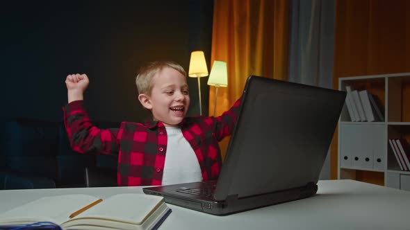 Happy Preschooler Raising Arms and Smiling While Celebrating Victory in Video Game on Laptop