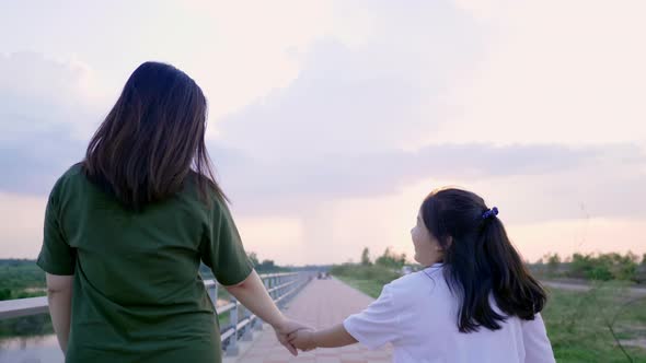 Back view of Asian mom and kid holding hand and walking outdoor