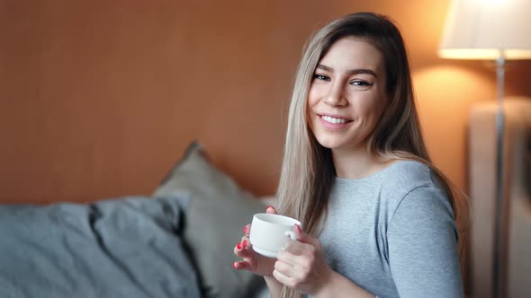 Portrait of Beautiful Mixed Race Blonde Girl Posing with Cup of Hot Tea at Cozy Bedroom