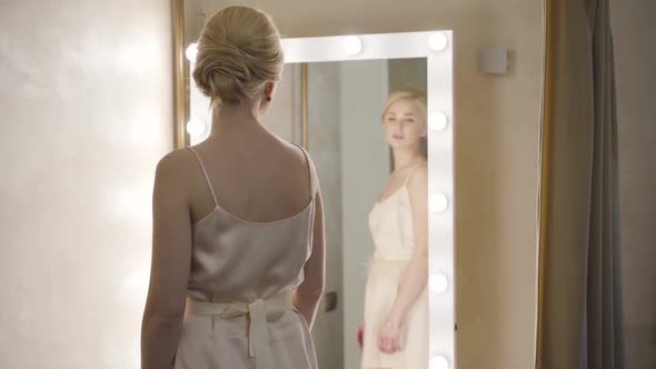 Back View of Elegant Young Lady Enjoying Reflection in Mirror in Dressing Room. Smiling Happy