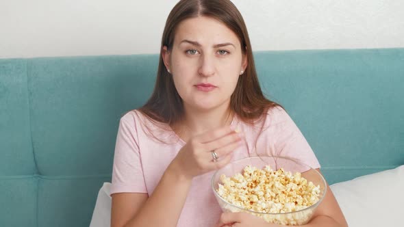 Portrait of Young Woman Wearing Pajamas Watching Television on Bed on Weekend and Eating Popcorn