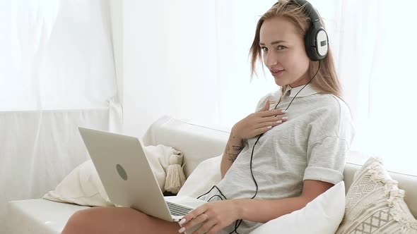 Girl is sitting white sofa in home with laptop happily talking over video link