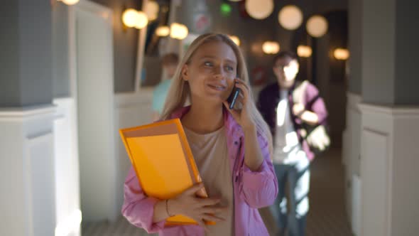 Happy Female Student Talks on Mobile Phone Walking Along University Corridor