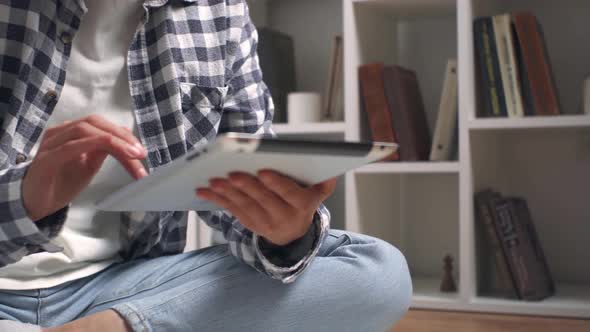 Holds A Tablet Serving On The Screen Of The Tablet. A Young Girl Sits On The Floor Without Socks