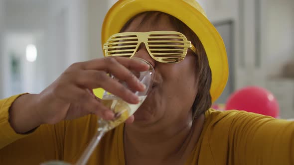 Happy african american senior woman drinking champagne and laughing making new year's eve video call